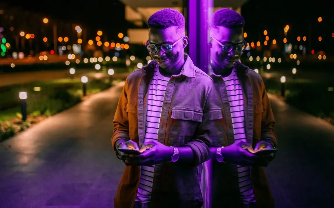 An artist and his reflection under purple light at night, both looking at their phones