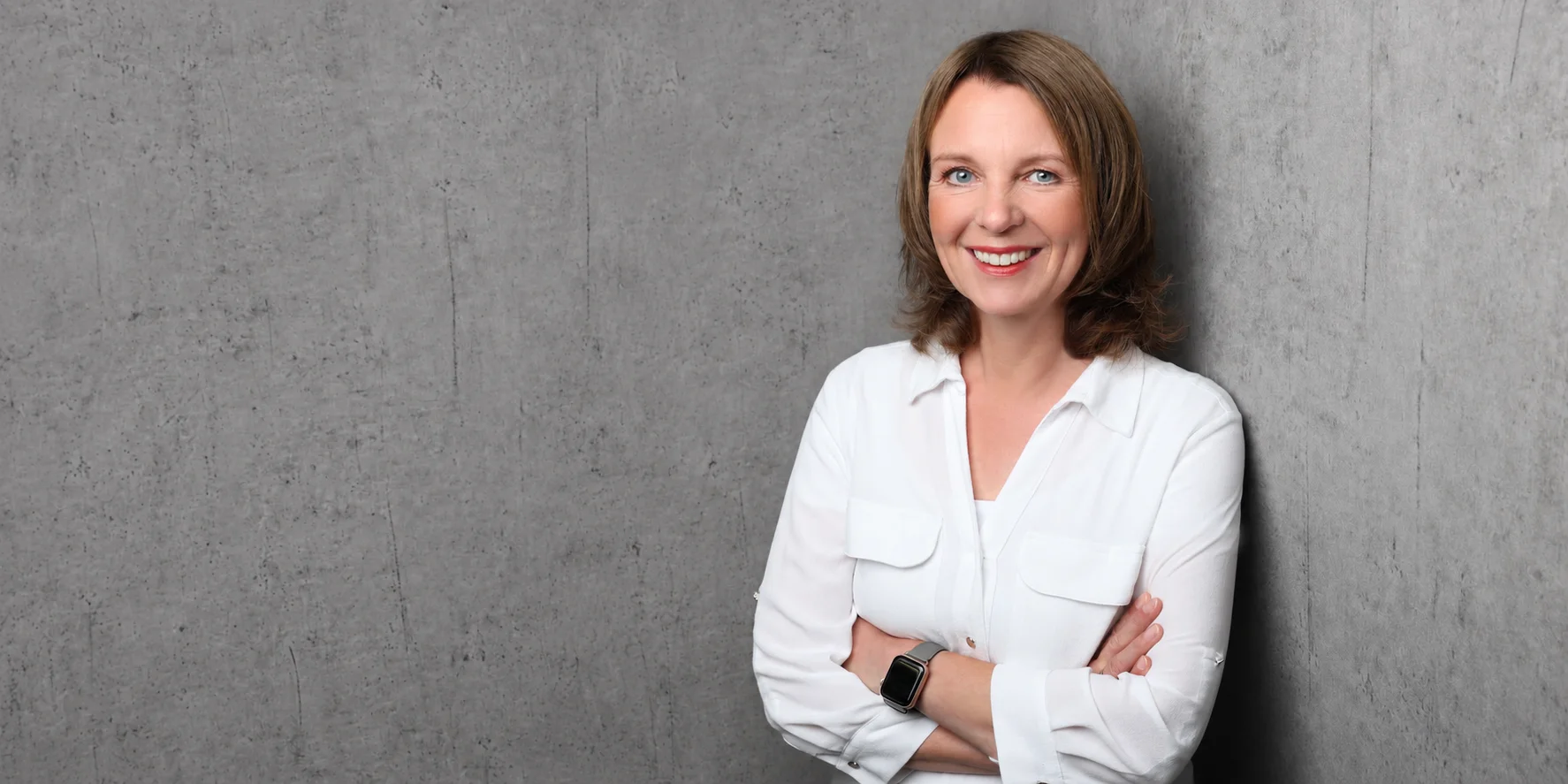 Andrea Palsherm of melino, smiling with her arms crossed against a grey concrete wall